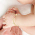 A baby's hand wearing the Good Luck Elephant Bracelet with Multicolor Birthstones gently rests on an adult's hand. In the background, the baby's toes are visible, adding to the heartwarming scene.